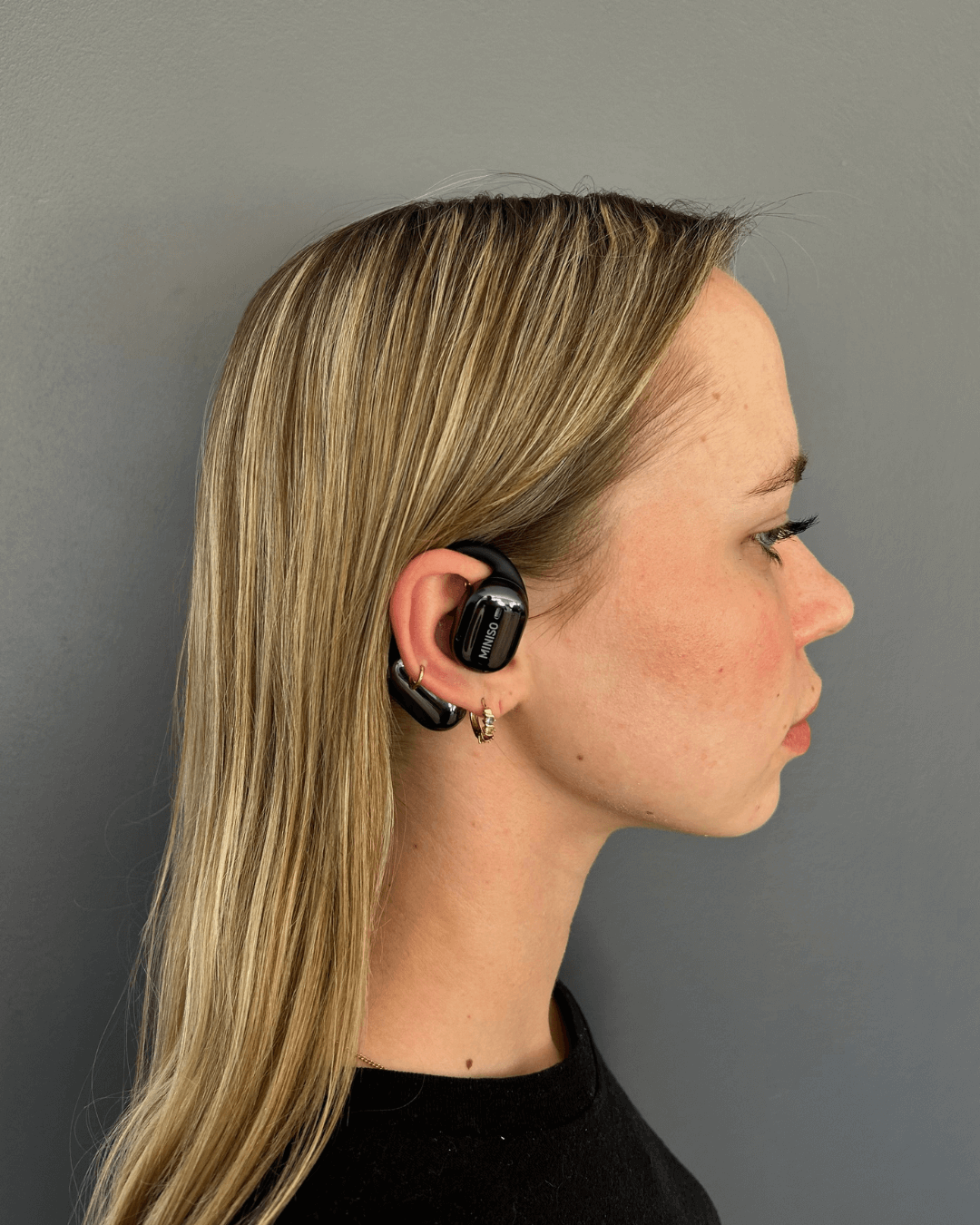 alt="Femme de profil portant un écouteur traducteur Hearific noir dans l’oreille droite"